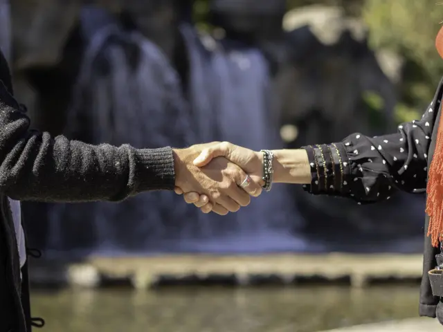 Two people shaking hands in front of a body of water