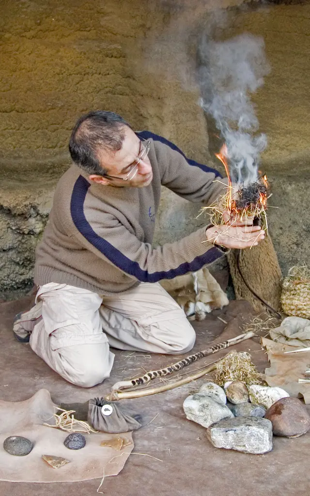 A man kneeling lights a ritual fire with ancient tools