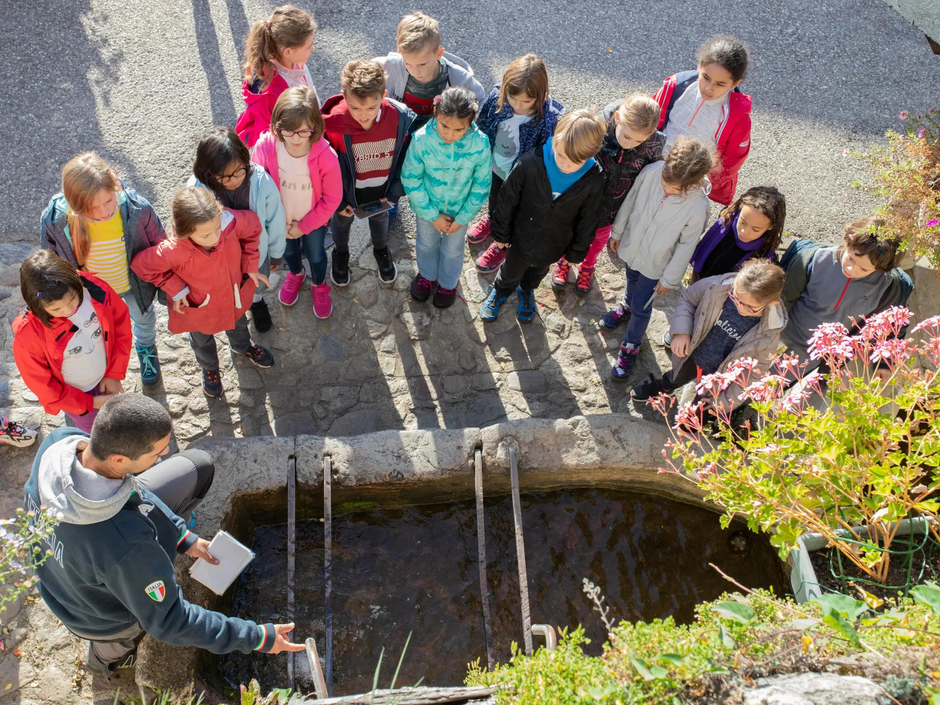 A group of children surrounding a natural spring with an adult