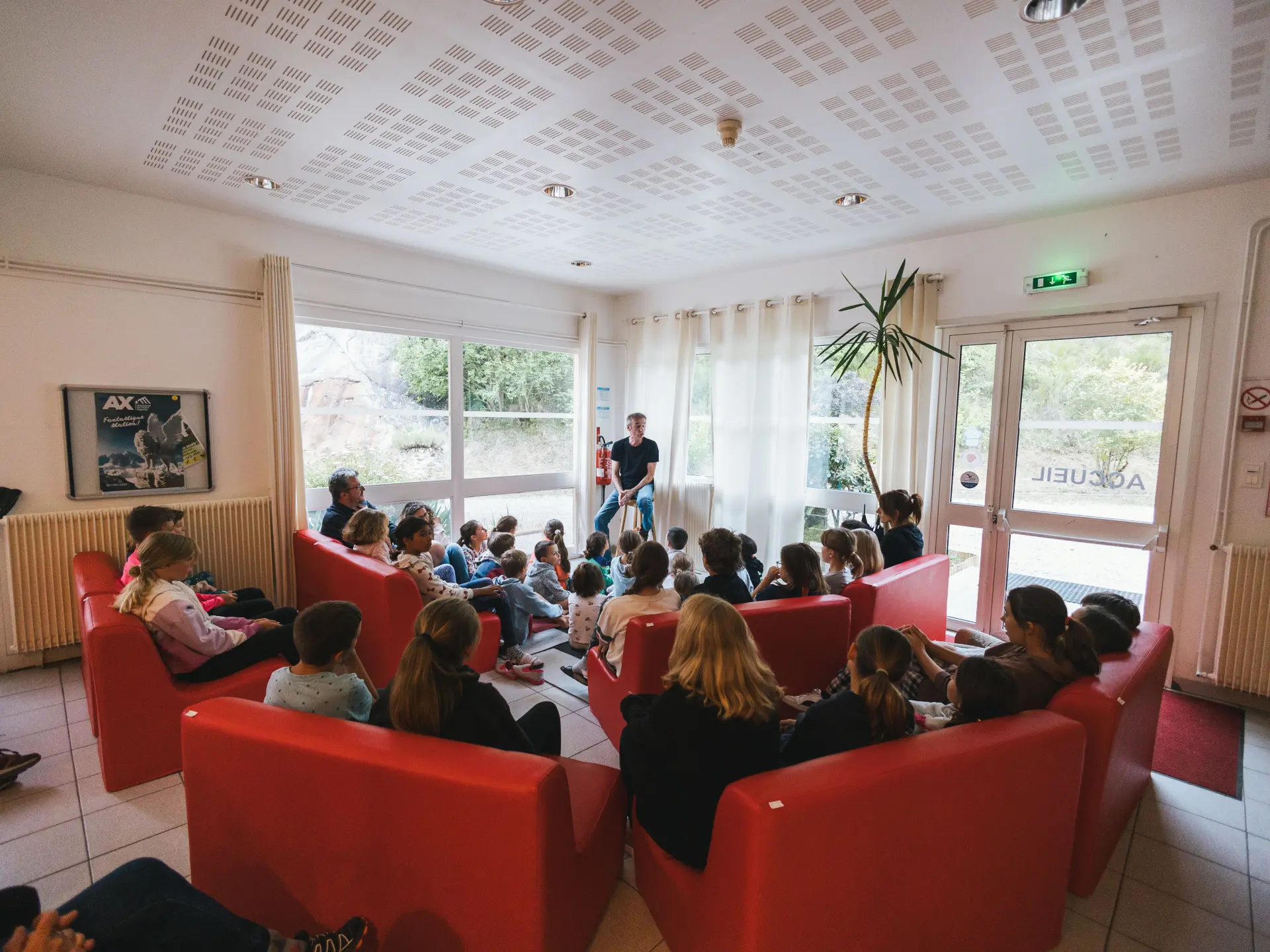 Niño de pie frente a un grupo de niños sentados en sofás rojos