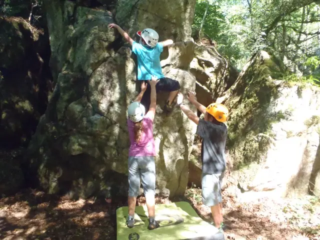 Three children climbing on a rock with protective helmets
