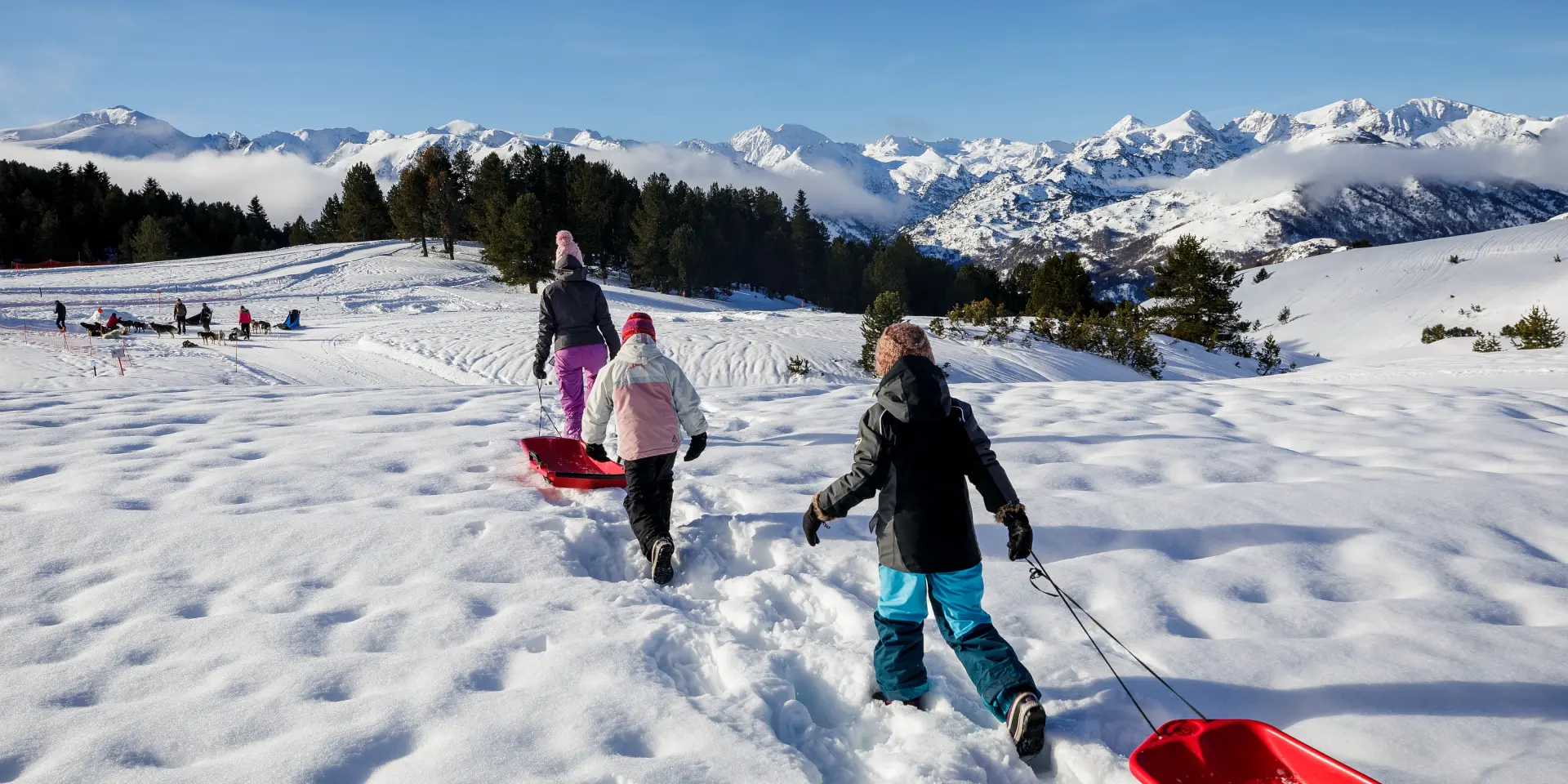 Children pulling sleds on a snowy slope with mountains in the background