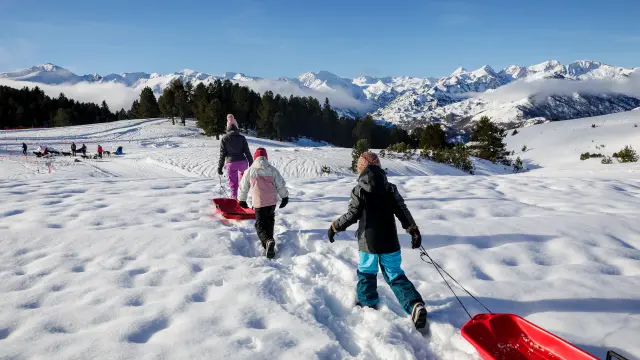 Children pulling sleds on a snowy slope with mountains in the background