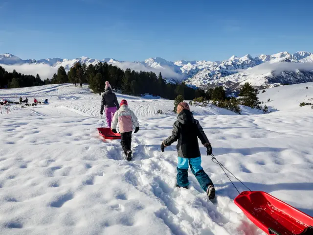 Enfants tirant des luges sur une pente enneigée avec des montagnes en arrière-plan