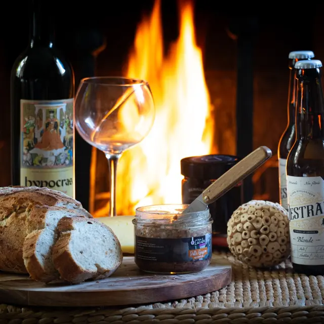 Un plateau avec du pain, du vin, de la bière et des accompagnements devant une cheminée