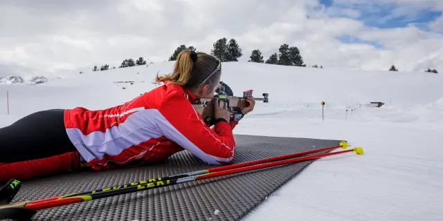 Une biathlète en position de tir sur un pas de tir enneigé