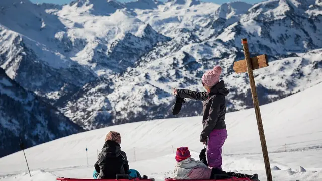 Deux enfants en train de faire du toboggan dans la neige avec des montagnes enneigées en arrière-plan
