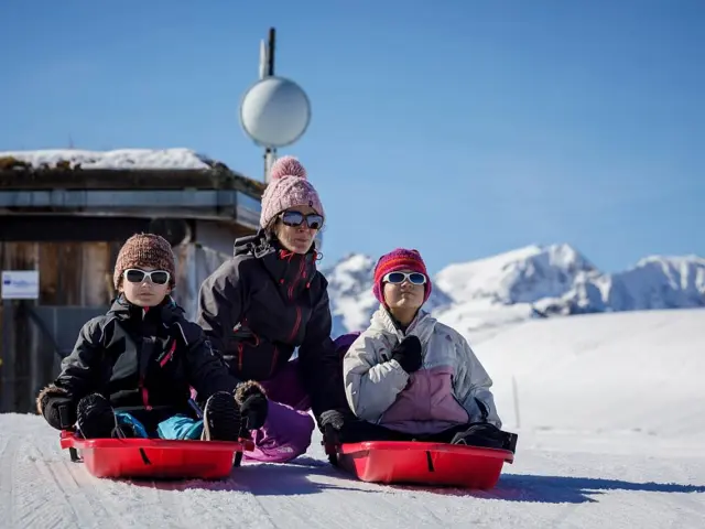 Trois personnes assises sur des luges rouges dans la neige