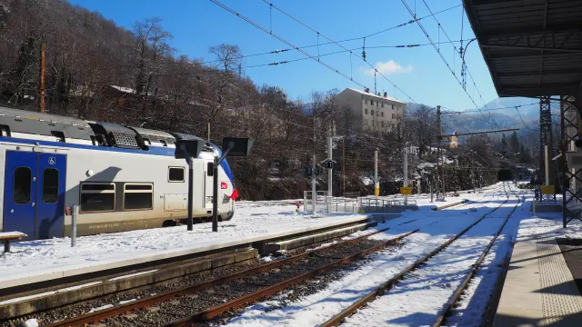 Train station avec un train arrêté sur les rails sous un ciel bleu avec des montagnes enneigées en arrière-plan
