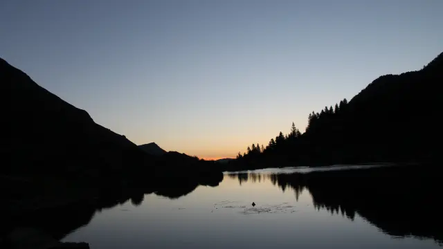 Couchant sur lac de montagne entouré de forêts et de montagnes