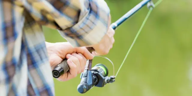 Mains tenant une canne à pêche près d'un plan d'eau