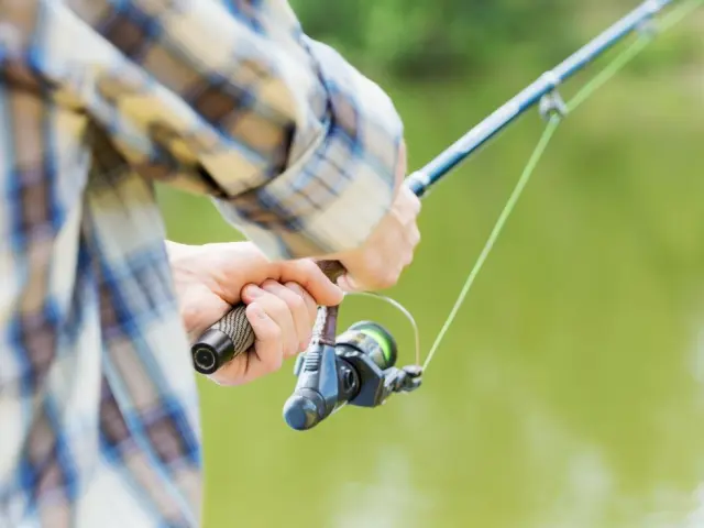 Mains tenant une canne à pêche près d'un plan d'eau