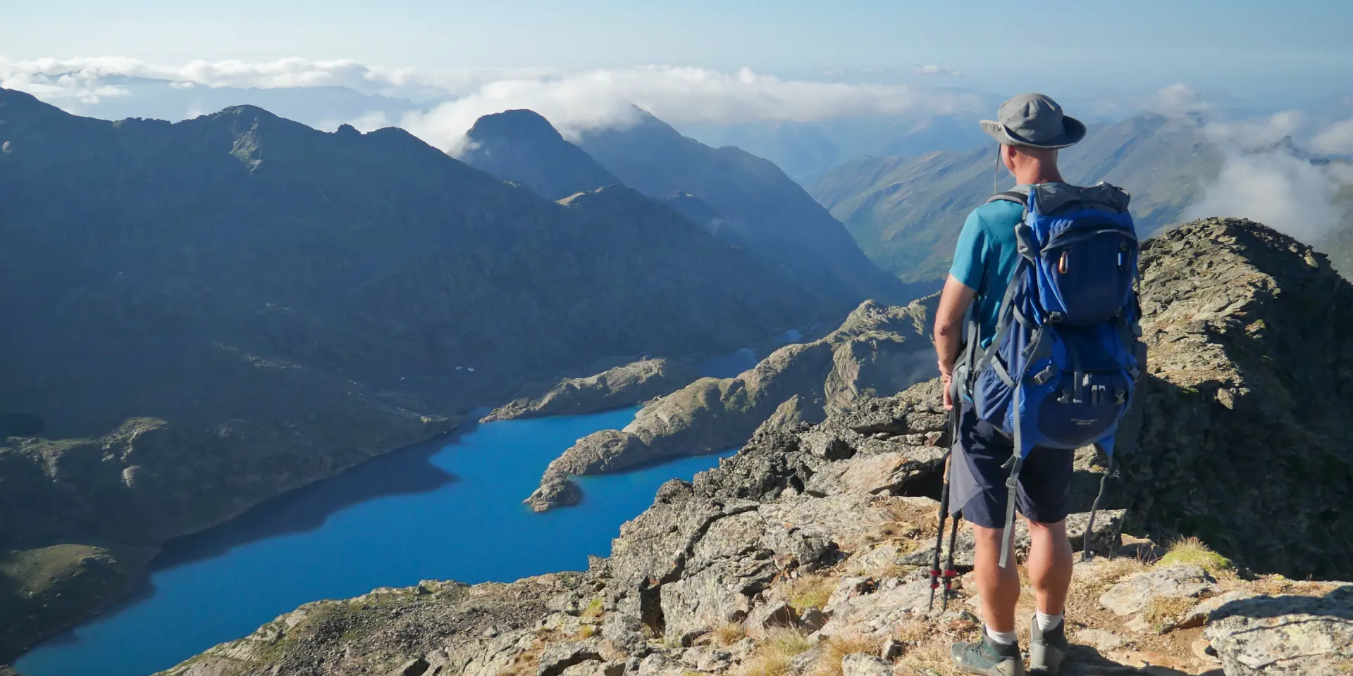 A hiker with a backpack on a mountain trail overlooking a lake