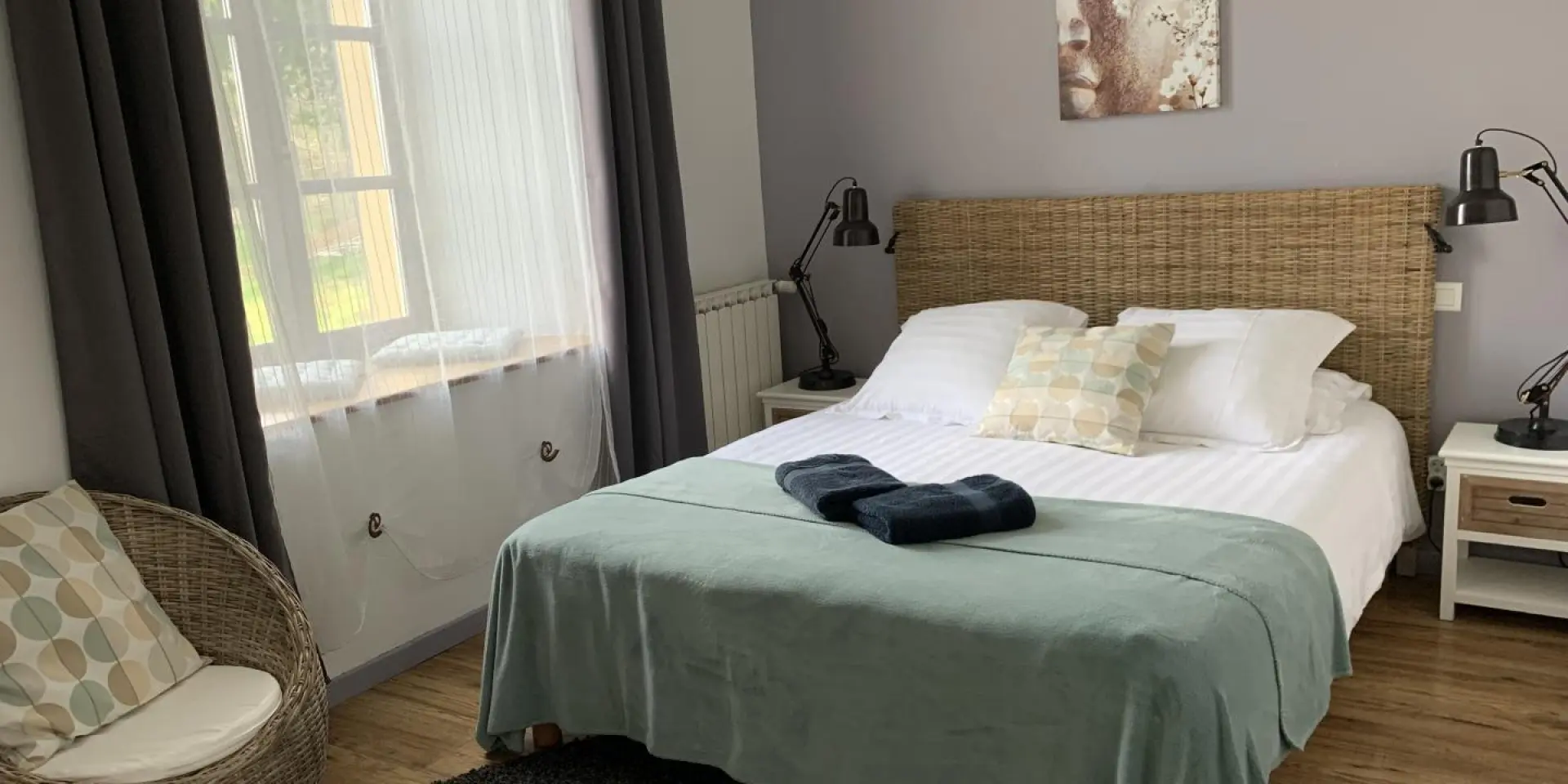 Bedroom with double bed, green blanket, two bedside lamps, and a window with gray curtains