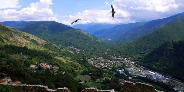 Village entouré de montagnes avec des vautours en vol