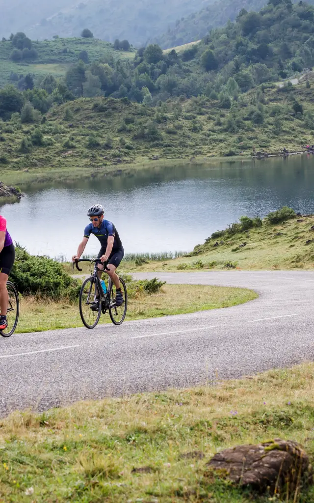 Deux cyclistes pédalent sur une route sinueuse près d'un lac de montagne