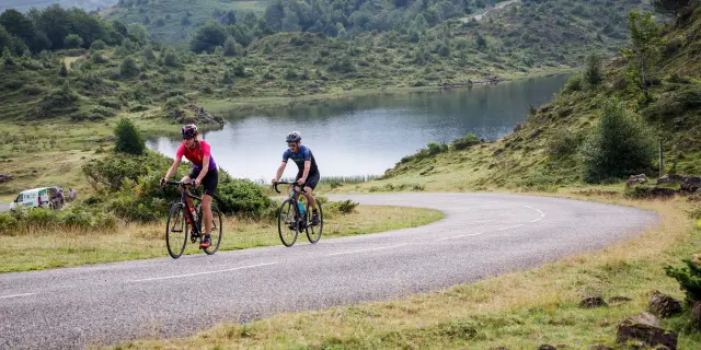 Deux cyclistes pédalent sur une route sinueuse près d'un lac de montagne