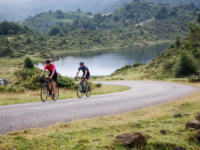 Deux cyclistes pédalent sur une route sinueuse près d'un lac de montagne