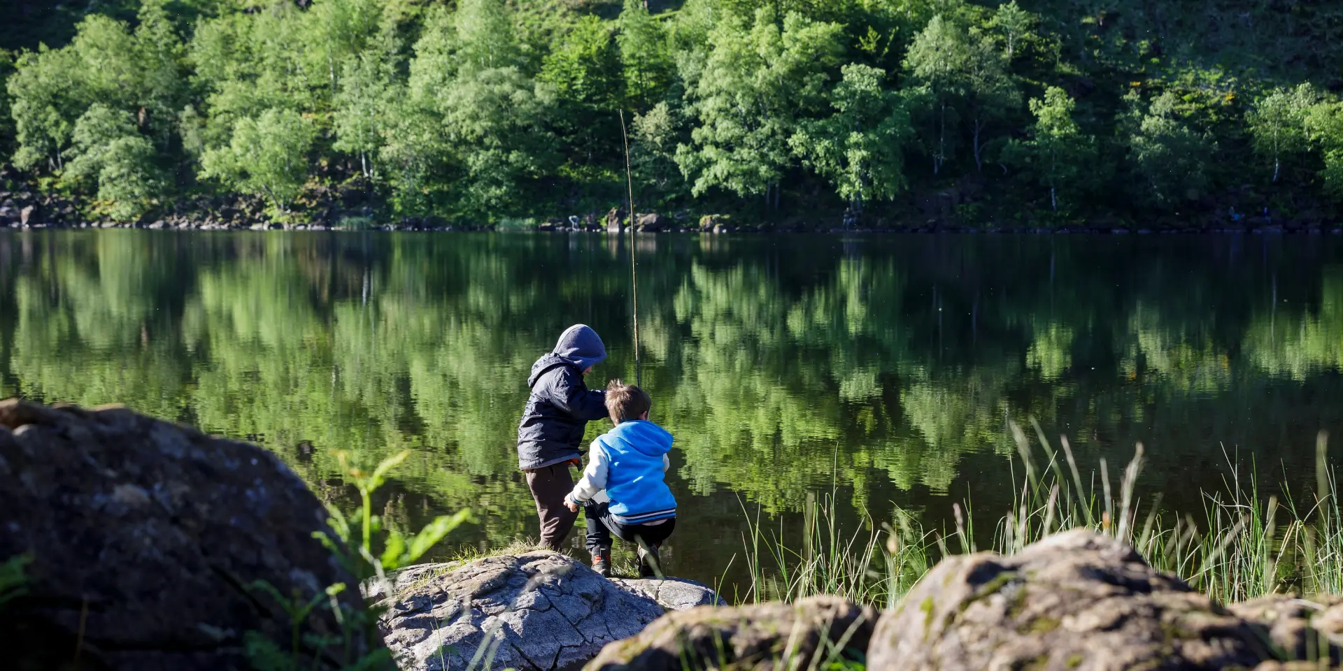 Un adulte et un enfant pêchent au bord d'un lac entouré d'arbres