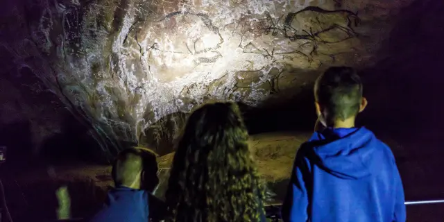 Trois personnes observent des peintures rupestres dans une grotte faiblement éclairée