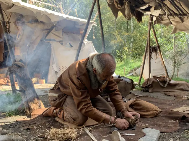 Un artisan travaille la pierre avec des outils primitifs sous un abri en peau