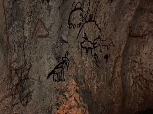 Stone wall with ancient rock carvings depicting human and animal figures