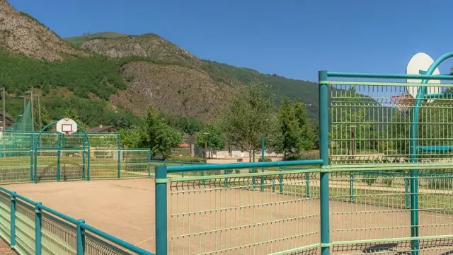 Terrain de basket entouré d'une clôture métallique avec des montagnes en arrière-plan