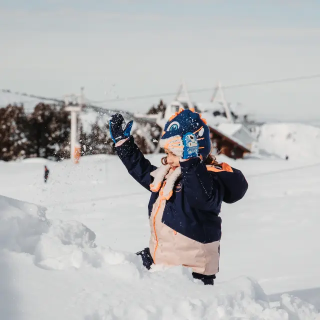 Niño vestido abrigado jugando en la nieve con guantes y una bufanda