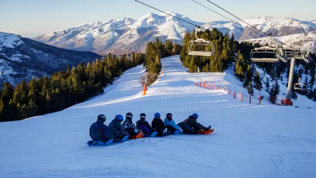 Group of snowboarders sitting on a snowy slope with ski lifts