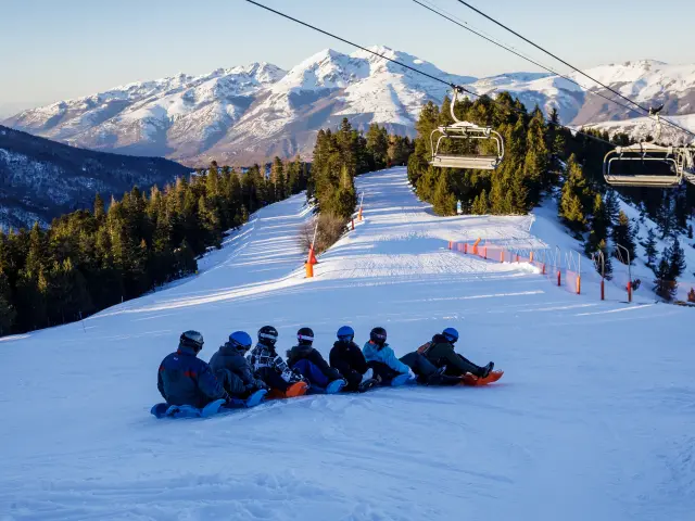 Groupe de snowboarders assis sur une pente enneigée avec des remontées mécaniques