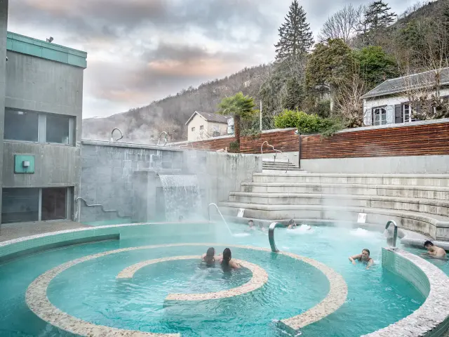 People relaxing in an outdoor hot spring bath surrounded by mountains