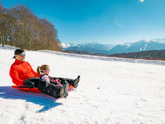 An adult and a child sliding down a snowy slope on a sled