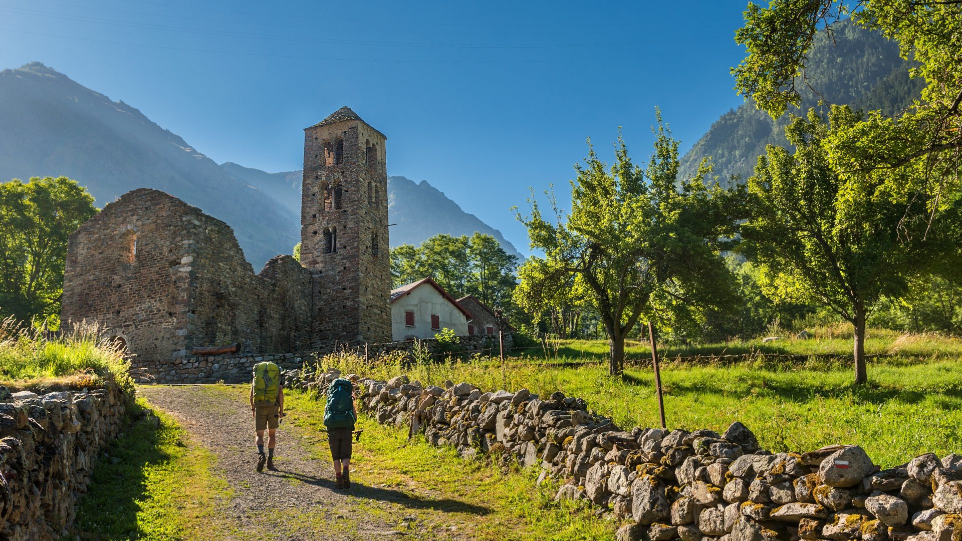 Two hikers walking on a dirt path near an old ruined church