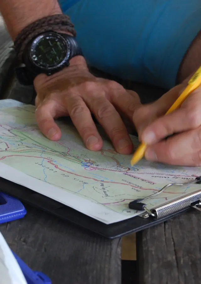 Une personne utilisant un crayon jaune pour marquer un sentier sur une carte dans un classeur.