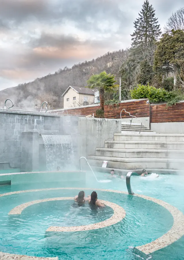 Personnes se baignant dans une piscine extérieure avec des montagnes en arrière-plan