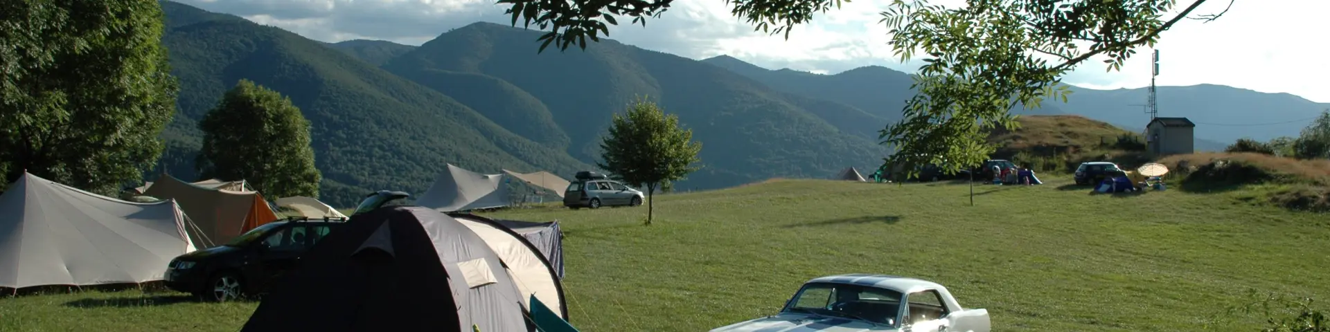 Tienda de campaña y coche en un camping en plena naturaleza con vistas a las montañas