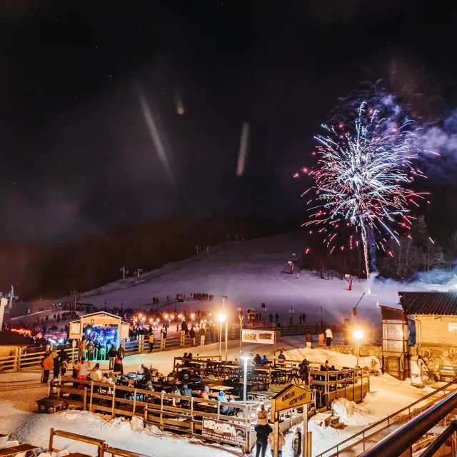 Feu d'artifice illuminant une station de ski enneigée la nuit