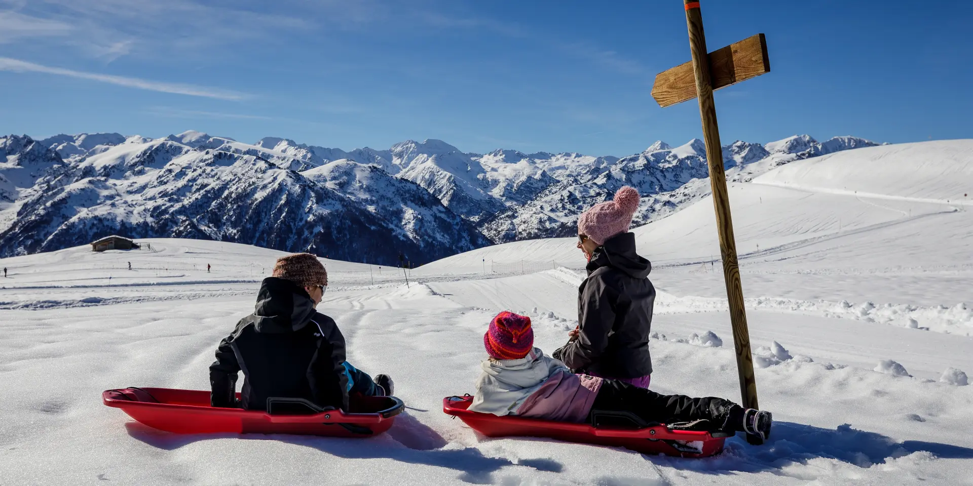 Trois enfants en luge sur une pente enneigée avec des montagnes en arrière-plan