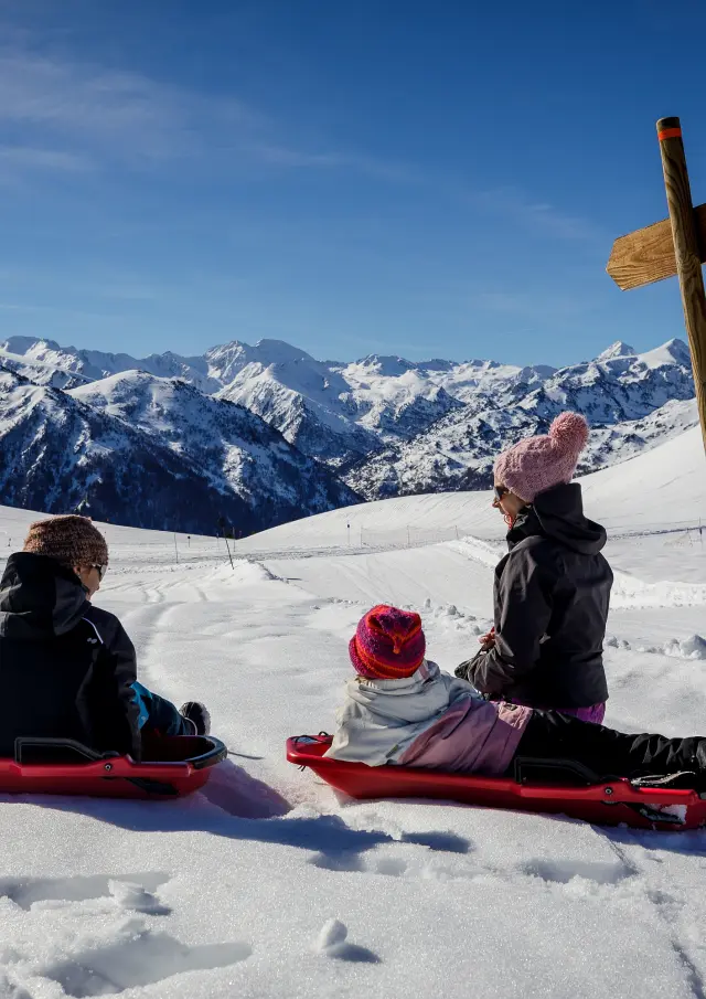 Trois enfants en luge sur une pente enneigée avec des montagnes en arrière-plan