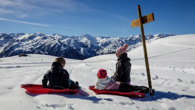 Trois enfants en luge sur une pente enneigée avec des montagnes en arrière-plan