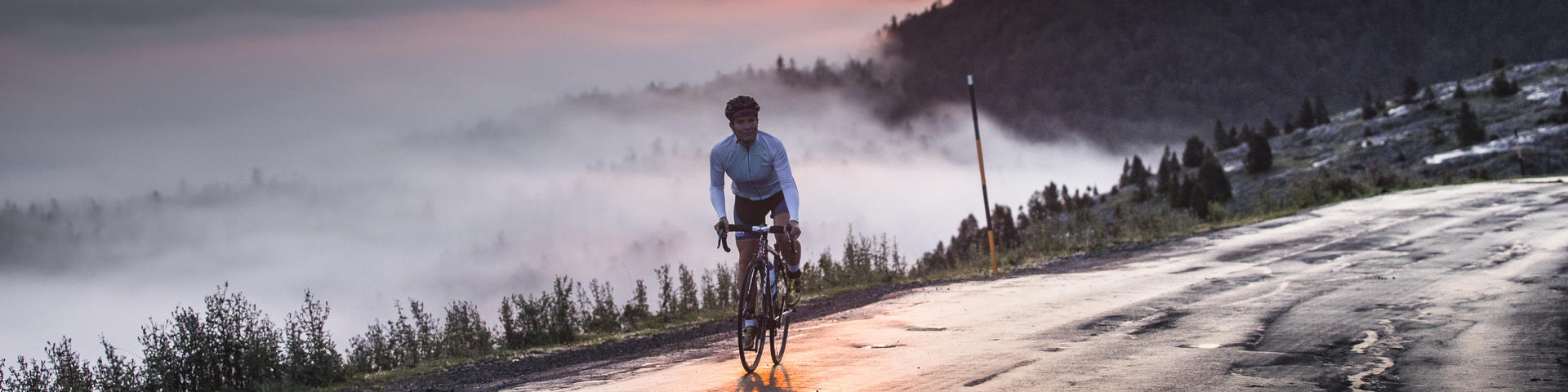 Une cycliste au sommet d'un col avec vue sur le coucher de soleil et les montagnes