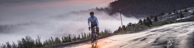 Une cycliste au sommet d'un col avec vue sur le coucher de soleil et les montagnes