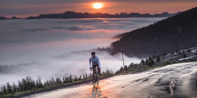 Une cycliste au sommet d'un col avec vue sur le coucher de soleil et les montagnes