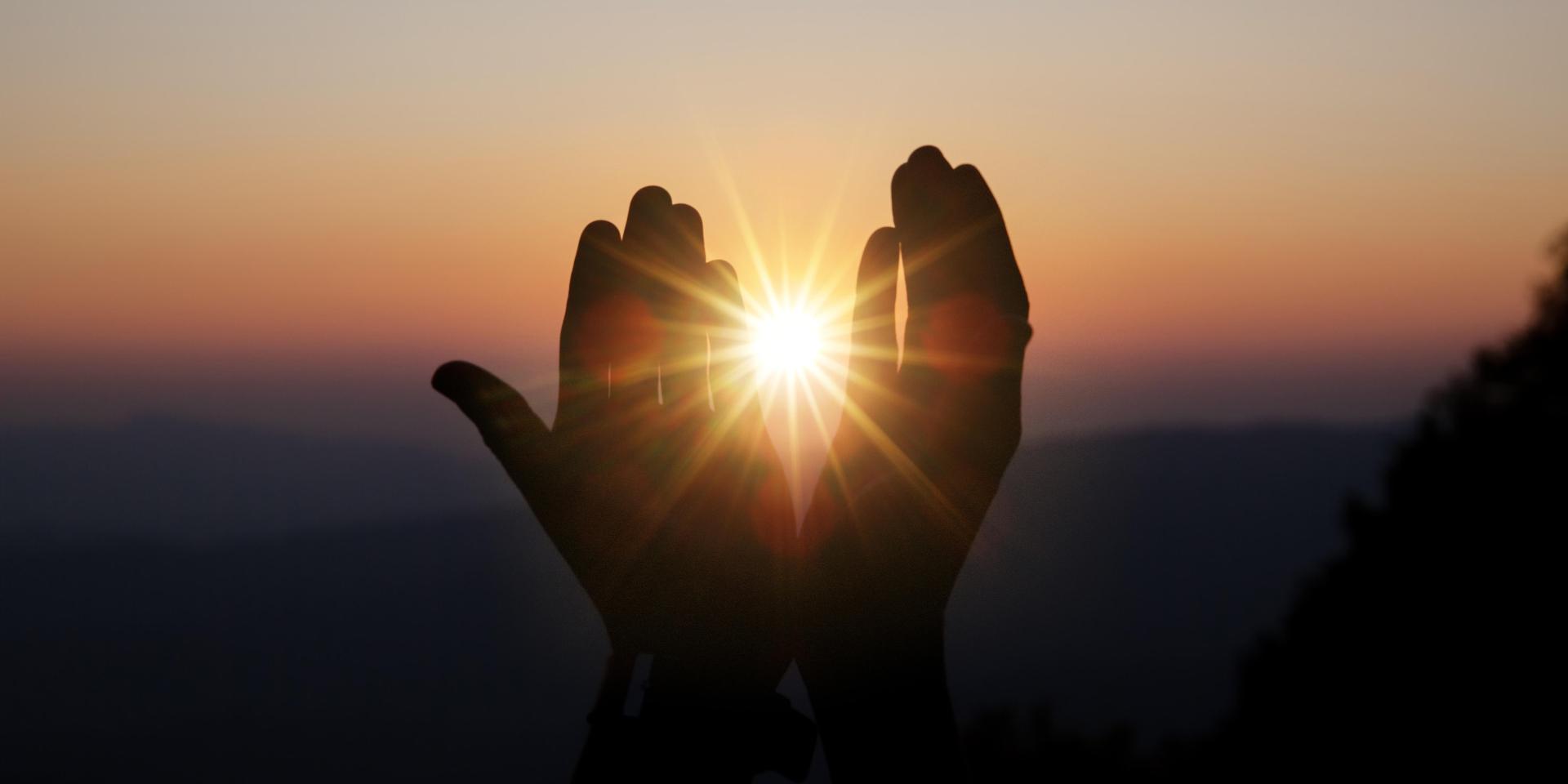 deux mains à trers lesquelles passent les derniers rayons du soleil à la fin d'une journée