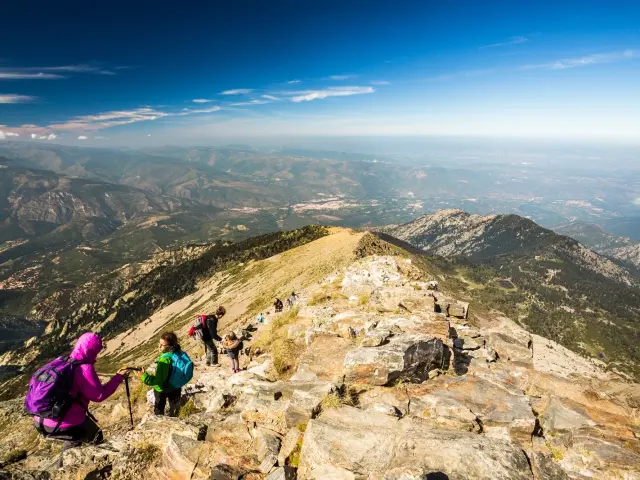 Randonneurs progressant sur les pentes rocailleuses du massif du Canigó, avec une vue panoramique sur les montagnes et la plaine des Pyrénées-Orientales.
