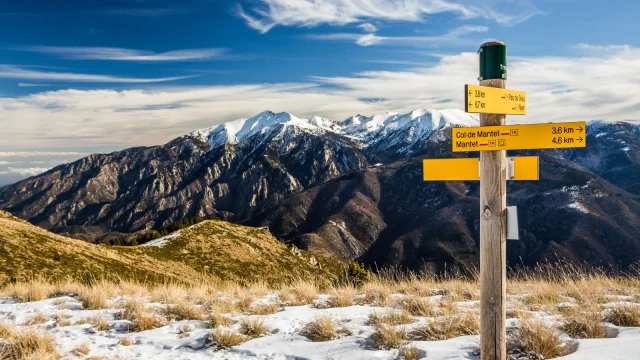 Panneau de randonnée en montagne indiquant le col de Mantet et Nyer, avec en arrière-plan le massif du Canigó enneigé sous un ciel bleu.