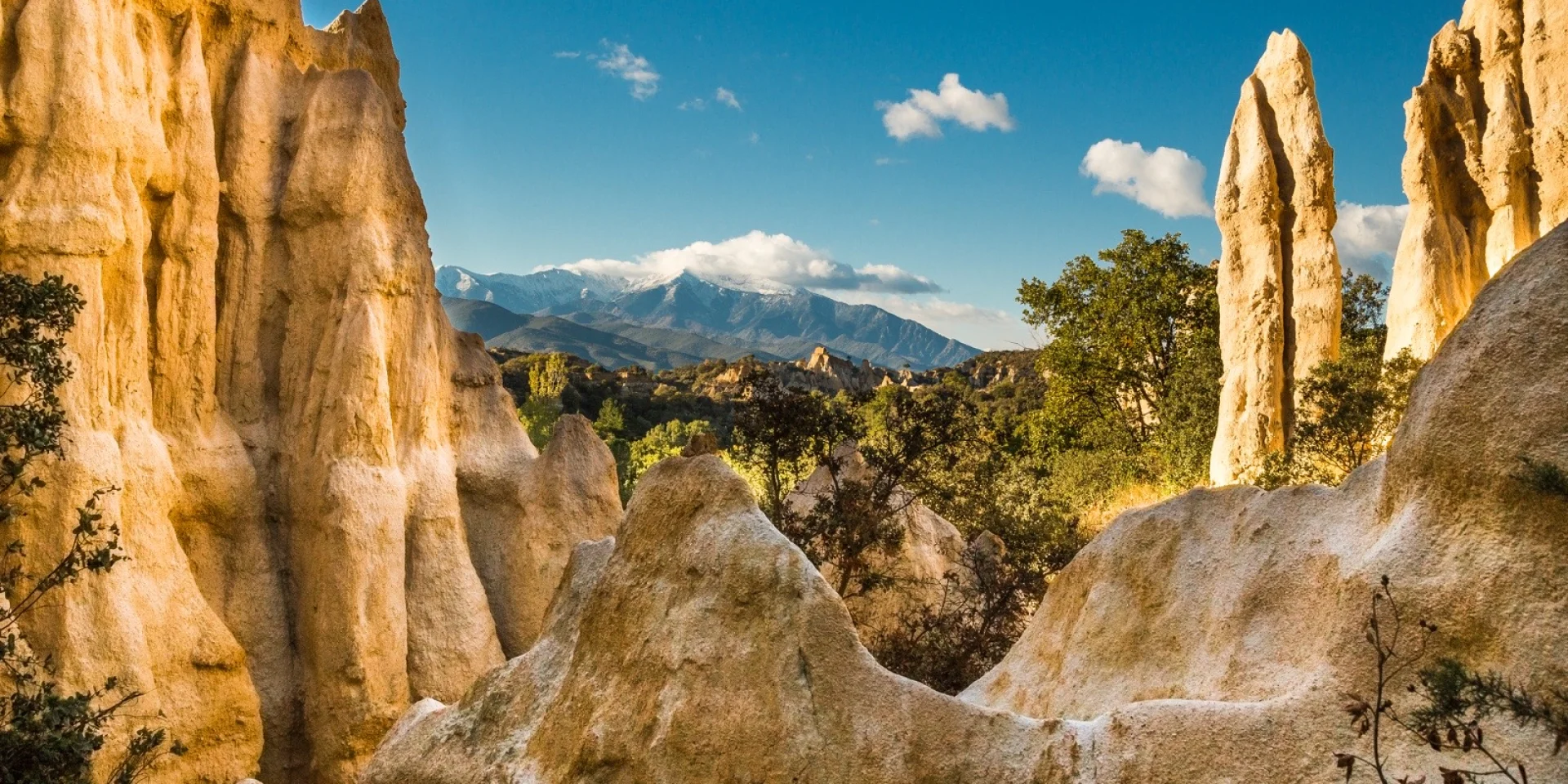 Formations rocheuses des orgues d’Ille-sur-Têt dans les Pyrénées-Orientales, avec vue sur le massif du Canigó enneigé sous un ciel bleu.