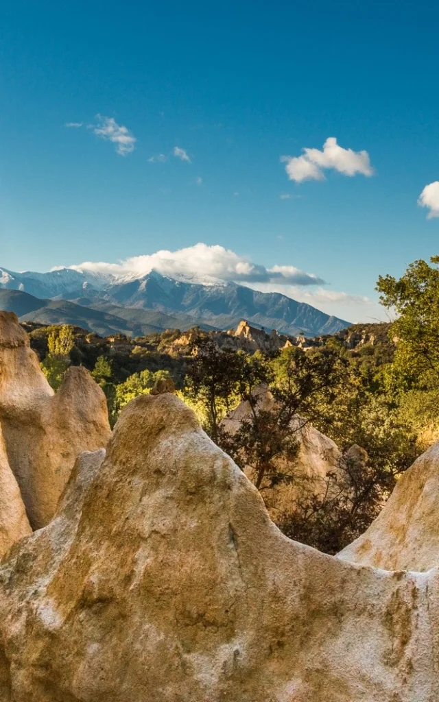 Formations rocheuses des orgues d’Ille-sur-Têt dans les Pyrénées-Orientales, avec vue sur le massif du Canigó enneigé sous un ciel bleu.