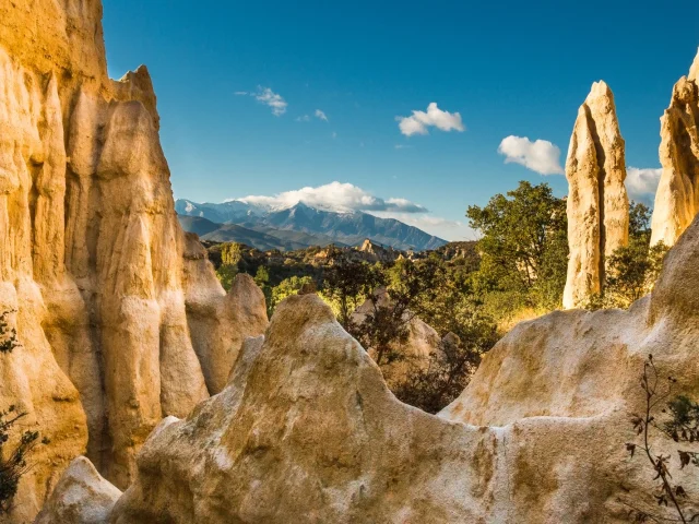 Formations rocheuses des orgues d’Ille-sur-Têt dans les Pyrénées-Orientales, avec vue sur le massif du Canigó enneigé sous un ciel bleu.