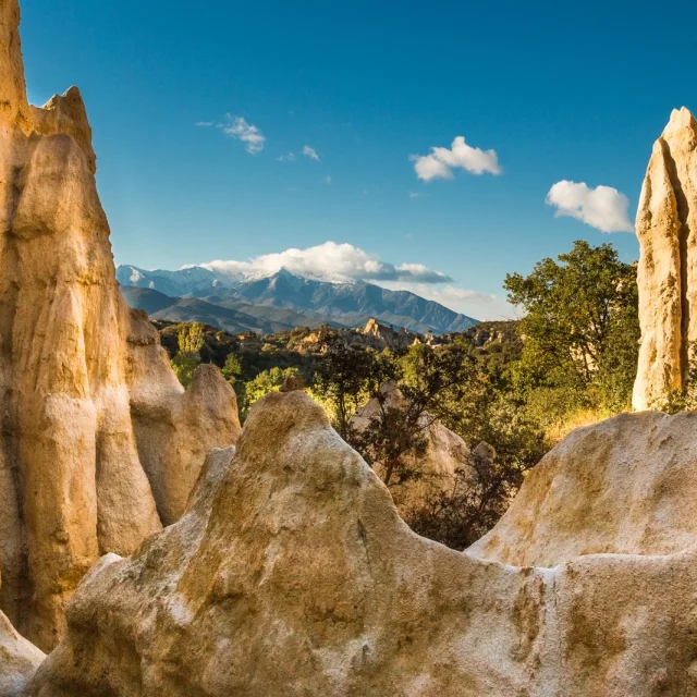Formations rocheuses des orgues d’Ille-sur-Têt dans les Pyrénées-Orientales, avec vue sur le massif du Canigó enneigé sous un ciel bleu.